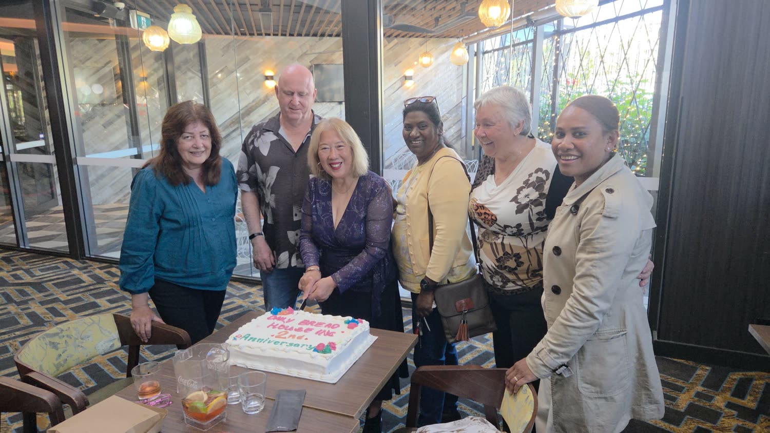 Daily Bread House founder Elsa Roache cutting the charity's second anniversary cake with volunteers.