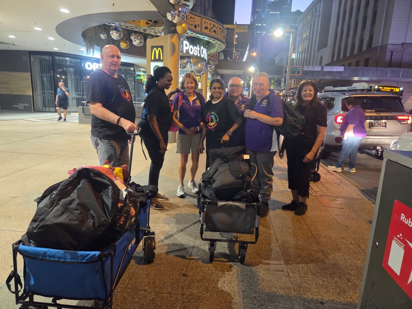 Volunteers with loaded wagons on a Brisbane city footpath at night.
